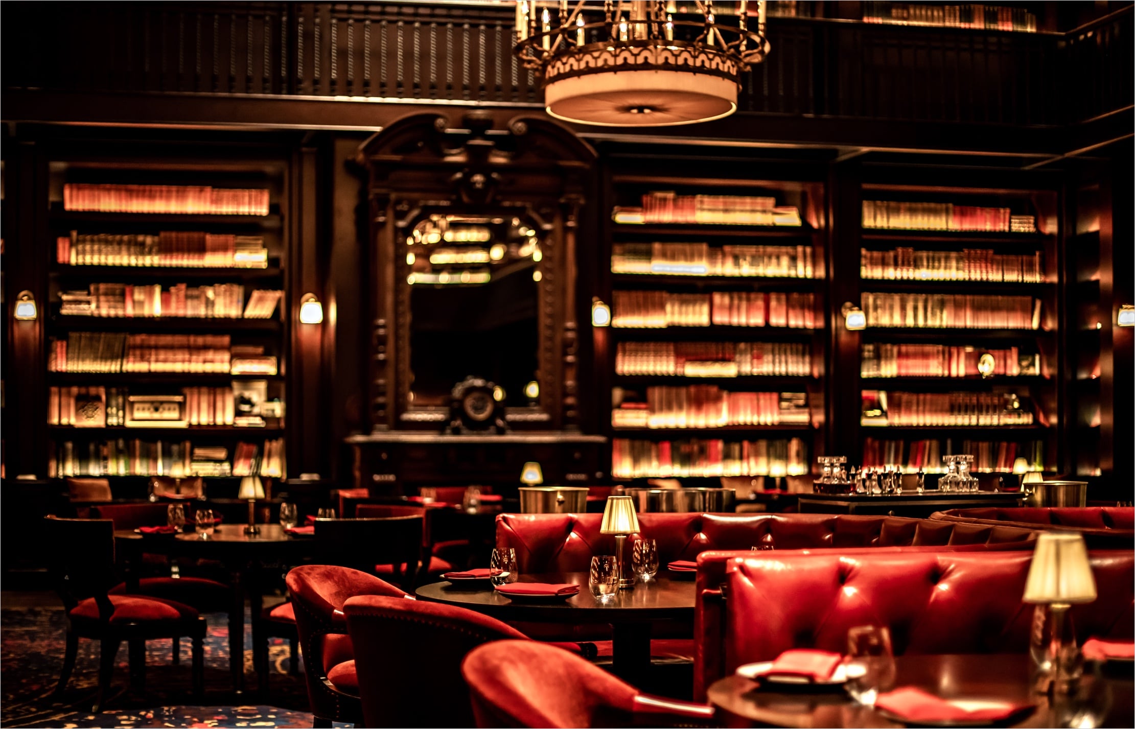 Interior view of The Restaurant, with dark wood dining tables and red velvet dining chairs, red leather tufted dining booths, and floor to ceiling bookshelves.